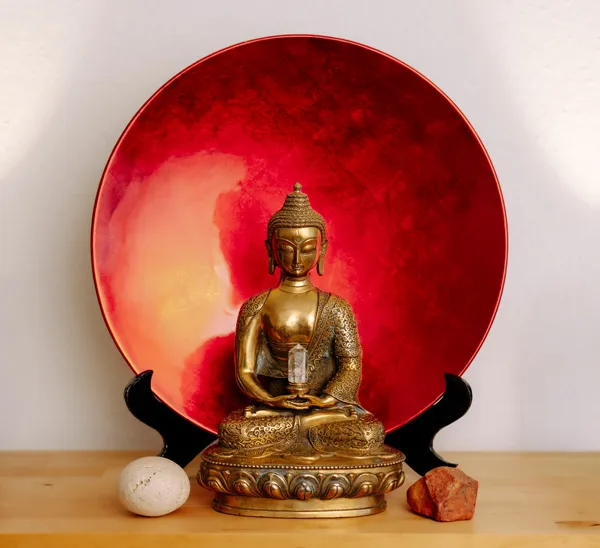 Buddha vor einer roten Schale, 2 Steine neben ihm links und rechts
