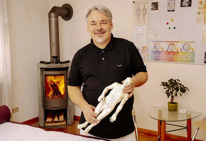 Rainer Weber im Praxisraum sitzend, Arme sind freundlich nach vorn gerichtet