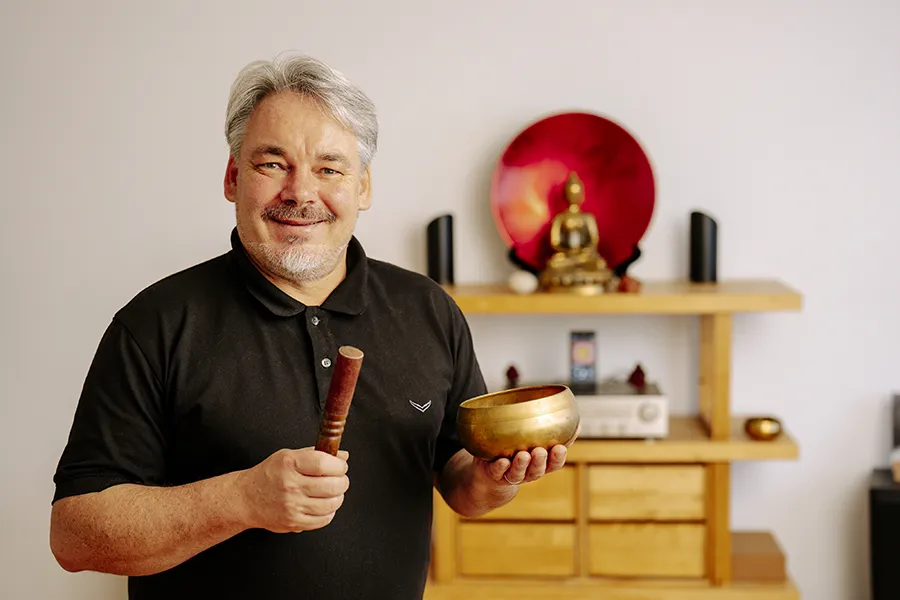 Rainer Webser hält eine goldene Klangschale und lächelt in die Kamera